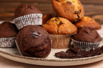 Plate with different muffins and chocolate on white wooden background, closeup