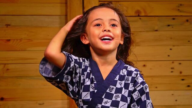 .A cute little boy sits in a wooden room, swaying his hair..slow motion A little boy with long flowing hair sits in a wooden room..A happy atmosphere with a wooden backdrop.
