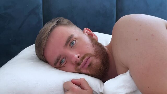 Sad sleepy depressed young handsome man is sleeping, exhausted tired person is suffering because of insomnia in bed in bedroom at night. Migraine, headache. Unhappy unhealthy guy.