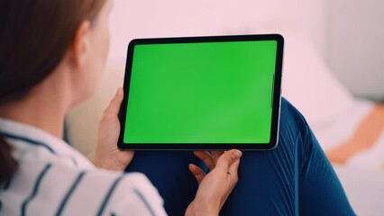 brunette woman sitting on the sofa holding digital tablet horizontal tap on green screen display weekend at home