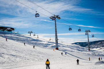 View of ski gondola and people skiing underneath it toward ski resort base at the end of the day  blue sky in background © Lana