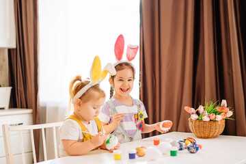 Little happy children draw Easter eggs in the kitchen. a little girl is laughing with an Easter egg in her hands. Easter holiday for children