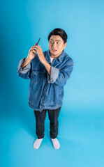 full body Young asian man using phone and posing on a blue background
