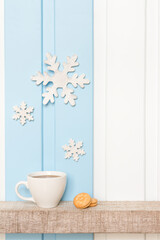 Winter decorations - Front view of Coffee cup with wooden snow flake and pines on shelf over blue white wall background .