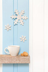 Winter decorations - Front view of Coffee cup with wooden snow flake and pines on shelf over blue white wall background .