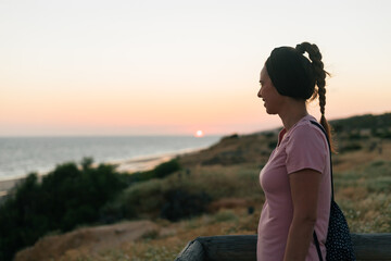 Naklejka na ściany i meble Happy girl traveling and enjoying the view of the lake or sea coast during majestic sunset