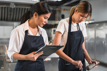 Asia woman assistant chef holding clipboard checking woman teenager cooking with kitchen background