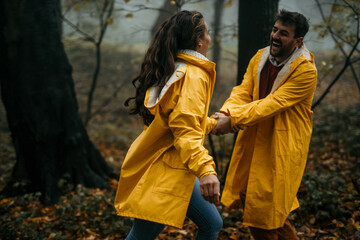 Naklejka na ściany i meble Loving couple in raincoats holding hands and having fun during a foggy day in the forest.