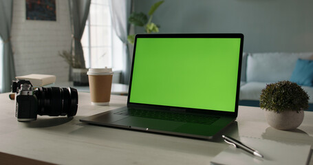The table of distant worker at home. Modern laptop computer with chroma key green screen. Remote work, distance learning, technology concept close up