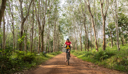 Woman smiling and bicycling through rubber tree forest on a dirt road