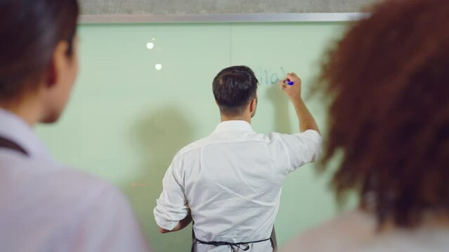 Male Teacher Explain to Students During Lesson About Project and Writting to Whiteboard. He explain equation point at whiteboard stand in classroom. Education, Chef, Learning, Lifestyle, Teching conce
