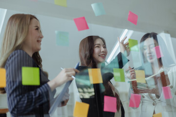 Team of asian business woman working with paper note on glass wall, Business people meeting to share idea at office, Business planning and Sticky note on glass wall.