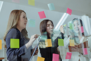 Team of asian business woman working with paper note on glass wall, Business people meeting to share idea at office, Business planning and Sticky note on glass wall.