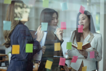 Team of asian business woman working with paper note on glass wall, Business people meeting to share idea at office, Business planning and Sticky note on glass wall.