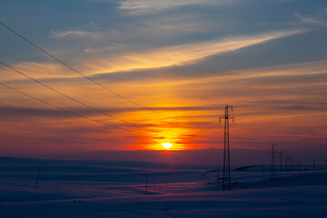 Fototapeta na wymiar electrical wires at sunset on a snow-covered ground