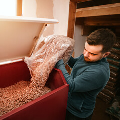 Sustainable future concept. Man is loading wood pellets into heating stove with bag. Heating...