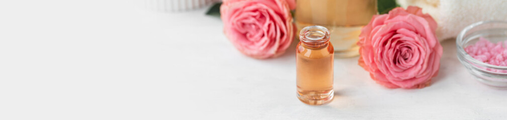 Aromatherapy. Pure organic essential rose oil concept. Elixir with plant based floral herbal ingredients. Pink flowers extract. Spa atmosphere with candle, towel. White background. Banner copy space