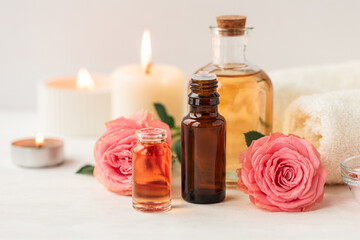 Fototapeta na wymiar Aromatherapy. Concept of pure organic essential rose oil. Elixir with plant based floral or herbal ingredients. Pink flowers extract. Spa atmosphere with candle, towel. White background