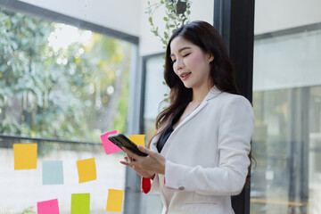 Asian businesswoman working on smartphone with sticky notes at the office.