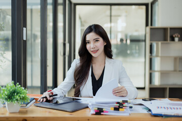 Joyful Asian businesswoman freelancer entrepreneur smiling and rejoices in victory while sitting at desk in office.