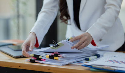 Asian business woman working with Stacks of paper files for searching, document on folders papers at desk office.