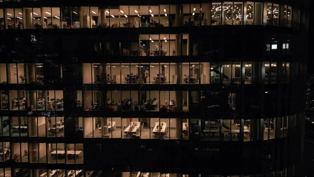 Stunning aerial view of an office building with illuminated empty offices shining bright at night close-up. Post-pandemic reality.