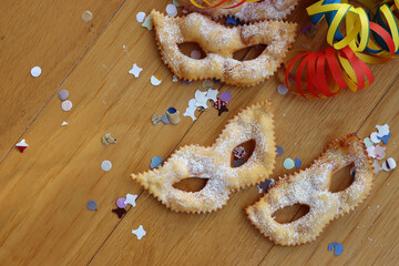 Traditional sweet crisp pastry deep-fried and sprinkled with sugar in shape of Carnival mask. Chiacchere or crostoli, bugie, cenci with confetti and paper serpentine. Copy space