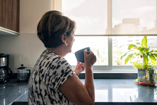 Mature Latin woman looking at the window drinking coffee