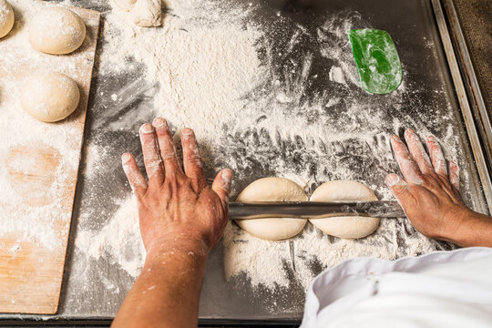Baker stretching uncooked round buns of bread with a metal roll