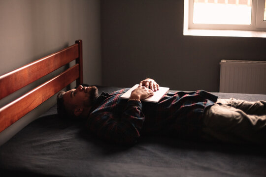 Exhausted man with laptop lying on bed at home