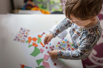 Blonde boy standing next to white table and doing art project