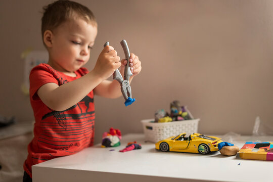 Upper body of small blonde boy playing with play doh with pilers