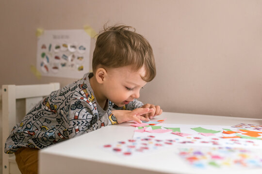 Blonde boy sitting on white chair next to white table and doing 