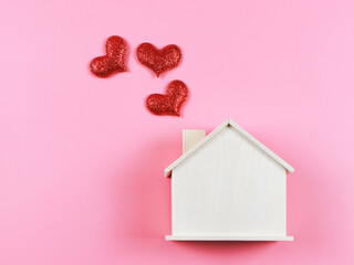 flat lay of wooden model house with red glitter hearts on pink  background. dream house , home of love, strong relationship, valentines.