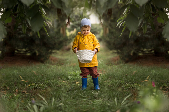 Boy in yellow raincoat, brown trausers and blue wellingtons hold