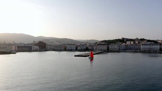 aerial drone shot of molo audace in trieste with red  sailboat passing by 