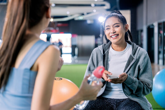 take a break in gym,asia female adult friend talking after working out laugh smile cheerful,two friend sit on ball conversation gossip hand show smartphone device screen positive facial expression