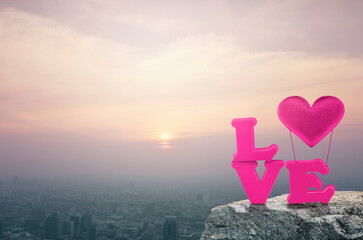 Pink love alphabet and fabric heart balloon on rock mountain over aerial view of cityscape at...