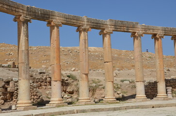 Fototapeta premium Sunny temples, arches, the Nymphaeum, stone ornaments, columns and column bases on the ruins of the city of Jerash in Jordan.