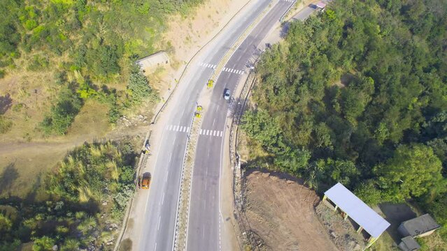 locked aerial drone shot showing car sanding on wide 4 lane highway in hills surrounded by forests and mountains in himachal pradesh on route to manali