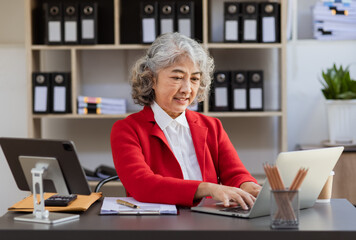 Asian senior woman using laptop computer and working planning at office desk.