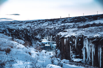 Iceland blue river with icicles cliffs in snowy winter landscape