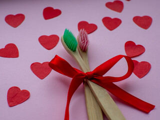 Flat lay with a lot of tiny heart-shaped papers, two toothbrushes and space for text. Red heart paper background with toothbrushes tied with a red bow. Valentines day dentist concept. February 14th.