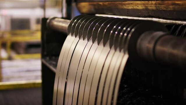 Dolly shot of metal strips hanging on roll slitting machinery in factory