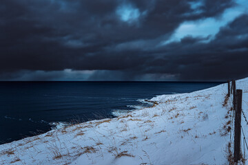 Iceland storm over the ocean with dark clouds and snow coastline