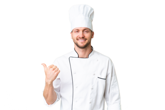 Young caucasian chef over isolated chroma key background pointing to the side to present a product