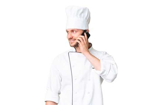Young caucasian chef over isolated chroma key background keeping a conversation with the mobile phone with someone