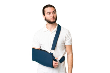 Young handsome man with broken arm and wearing a sling over isolated chroma key background looking to the side