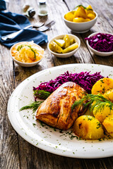 Fried pork loin with boiled potatoes and red cabbage on wooden table
