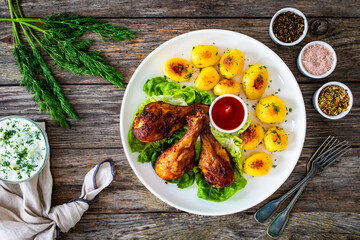 Barbecue chicken drumsticks with fried potatoes, lettuce and ketchup on wooden table
